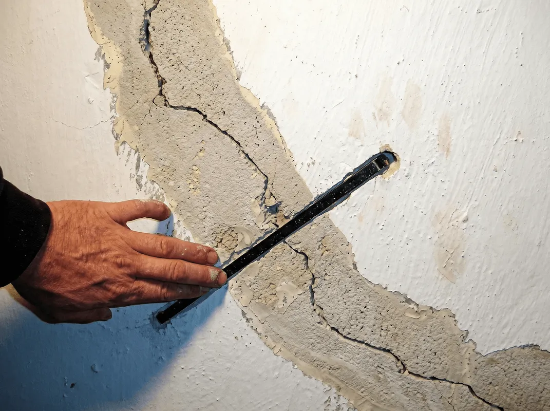 A wall with a large crack is being inspected by a professional in Kansas City, KS